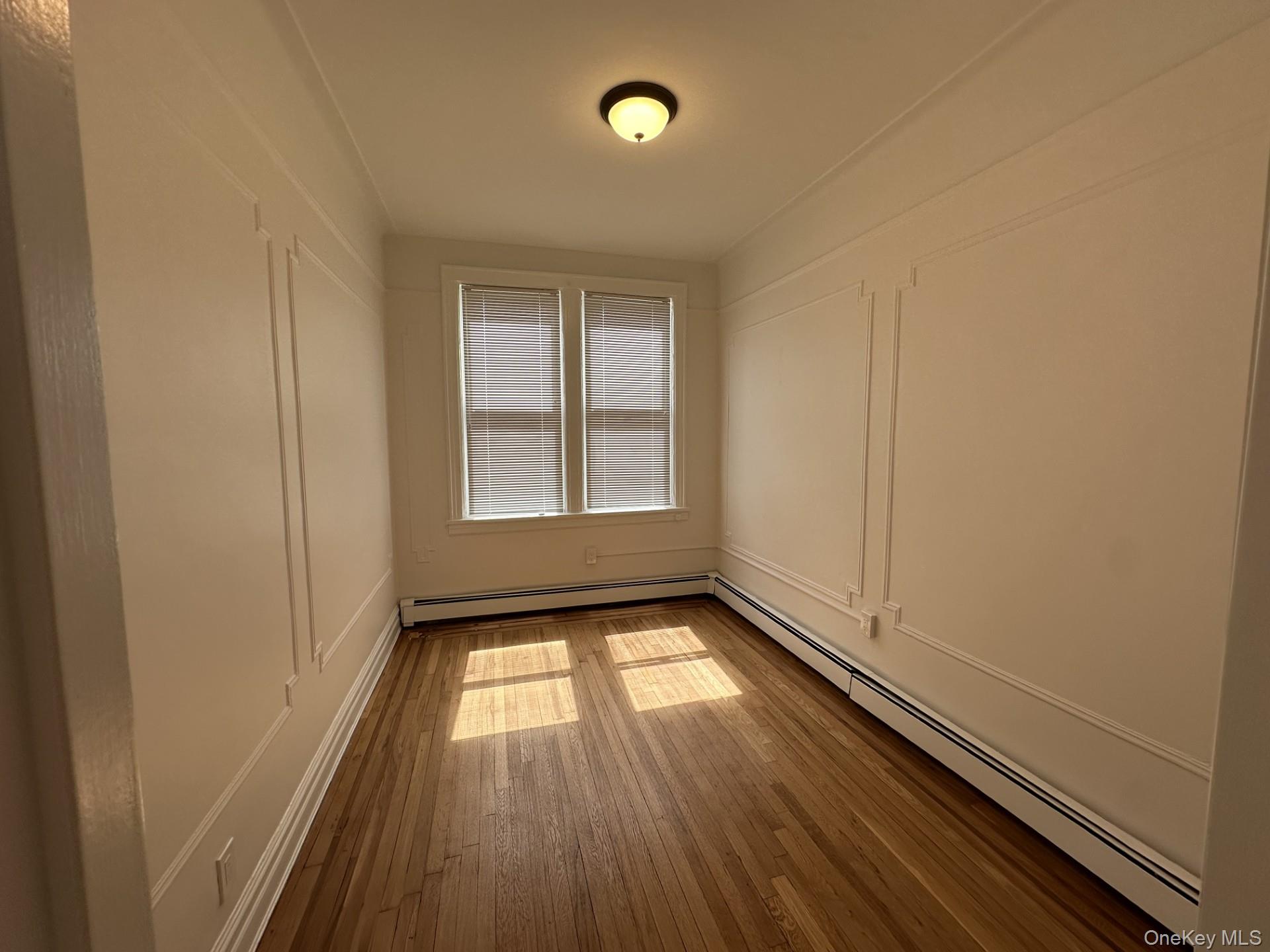 117 Plandome Road, Unit 2R Manhasset, NY 11030 - Photo 10 of 13 Bedroom featuring baseboard heating, a decorative wall, and hardwood floors