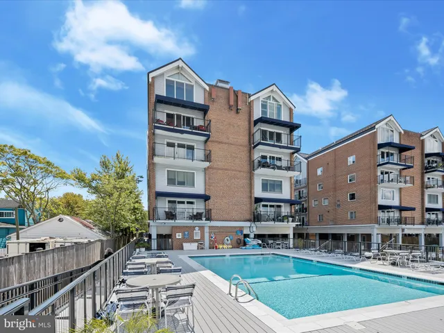 a front view of a residential apartment building with a yard and large trees