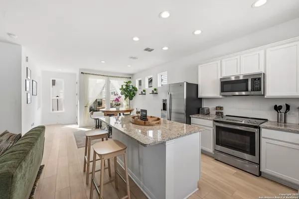 a open kitchen with stainless steel appliances granite countertop a stove top oven a sink dishwasher a dining table and chairs with wooden floor