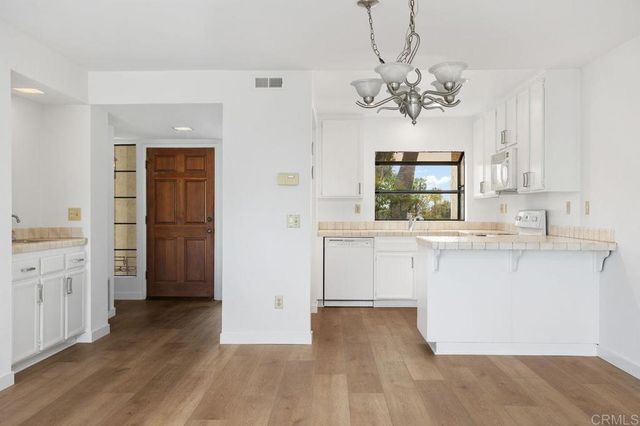 a kitchen with kitchen island a sink dishwasher a refrigerator with white cabinets and wooden floor