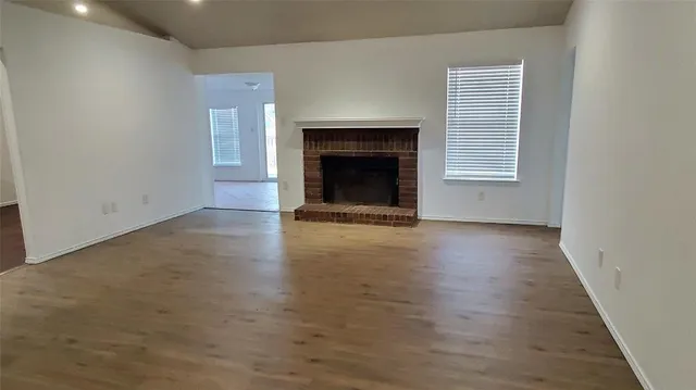an empty room with wooden floor fireplace and windows