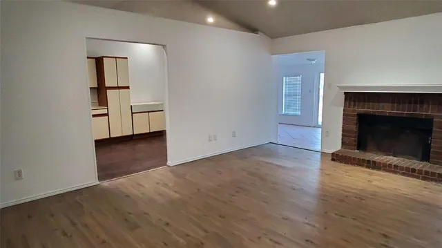 an empty room with wooden floor fireplace and windows