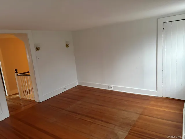 a view of an empty room with wooden floor and a hallway
