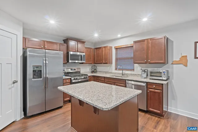 a kitchen with stainless steel appliances granite countertop a stove top oven a refrigerator a sink and dishwasher with wooden floor