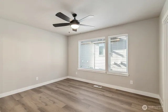 an empty room with wooden floor fan and windows