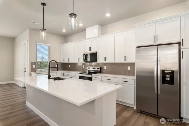 a kitchen with stainless steel appliances a refrigerator a stove a sink a center island and chairs with wooden floor