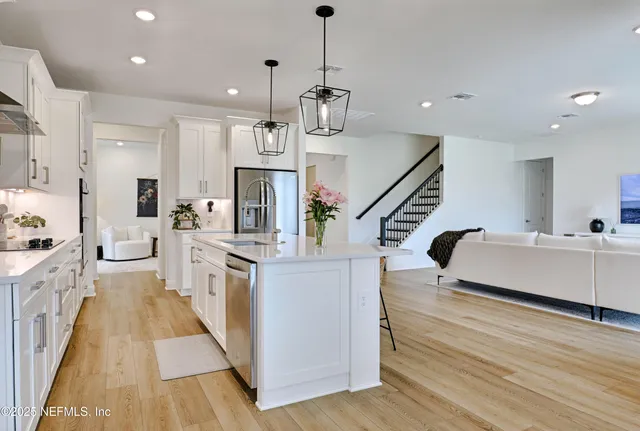 a kitchen with stainless steel appliances kitchen island granite countertop a refrigerator a oven and white cabinets with wooden floor