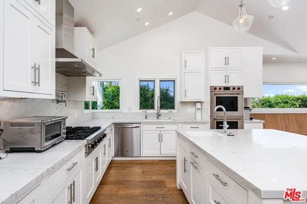 a large kitchen with kitchen island a large counter space a sink appliances and a large window