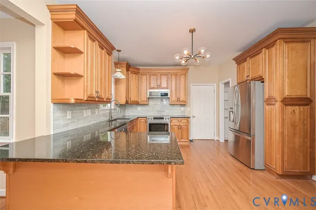 a kitchen with stainless steel appliances granite countertop a refrigerator a stove and a sink with wooden floor