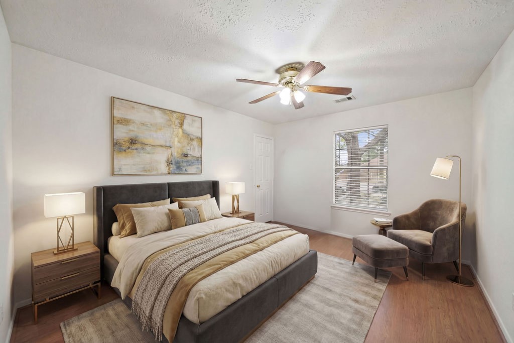 16114 Kintyre Point Road Houston, TX 77095 - Photo 34 of 44 This cozy bedroom features a large bed with neutral bedding, stylish nightstands with modern lamps, and a comfortable chair with an ottoman. The room has a ceiling fan, a window for natural light, and tasteful wall art, creating a welcoming atmosphere.