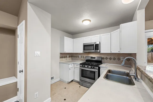 a kitchen with stainless steel appliances a sink a stove a microwave a refrigerator a stove and white cabinets