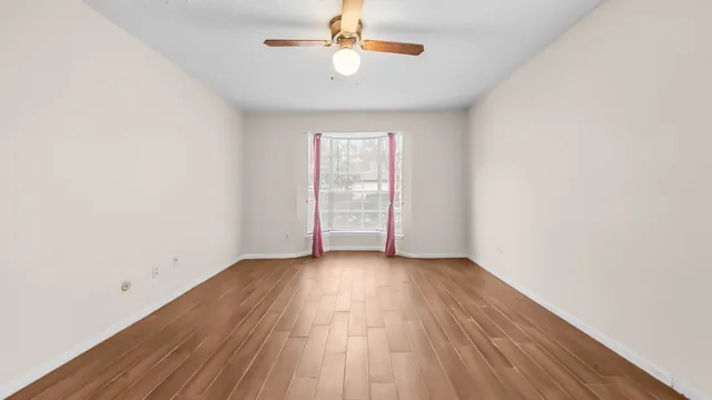 an empty room with wooden floor and a ceiling fan
