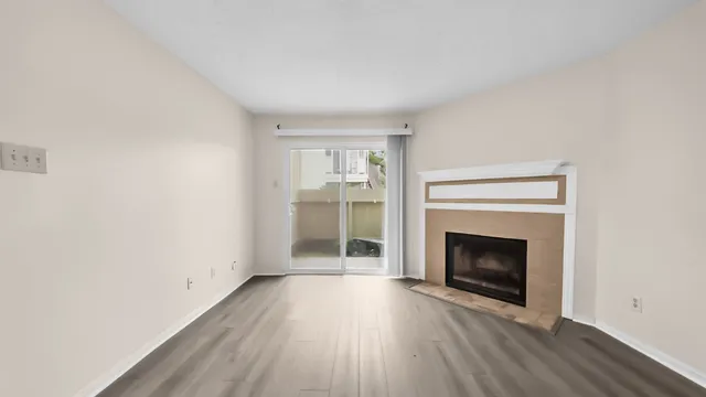 a view of an empty room with wooden floor fireplace and a window