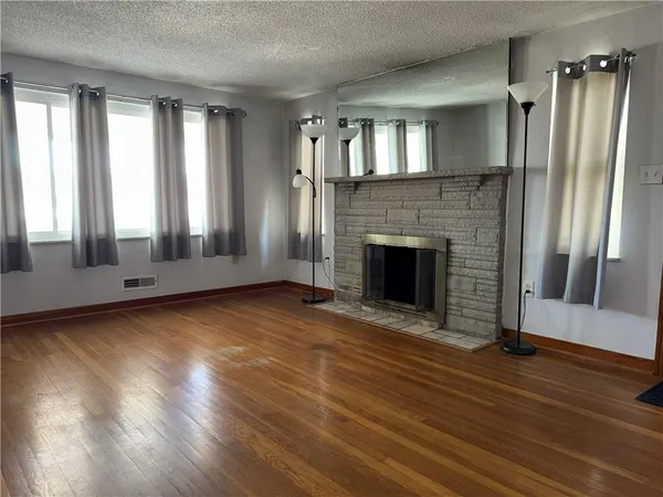 an empty room with wooden floor fireplace and windows