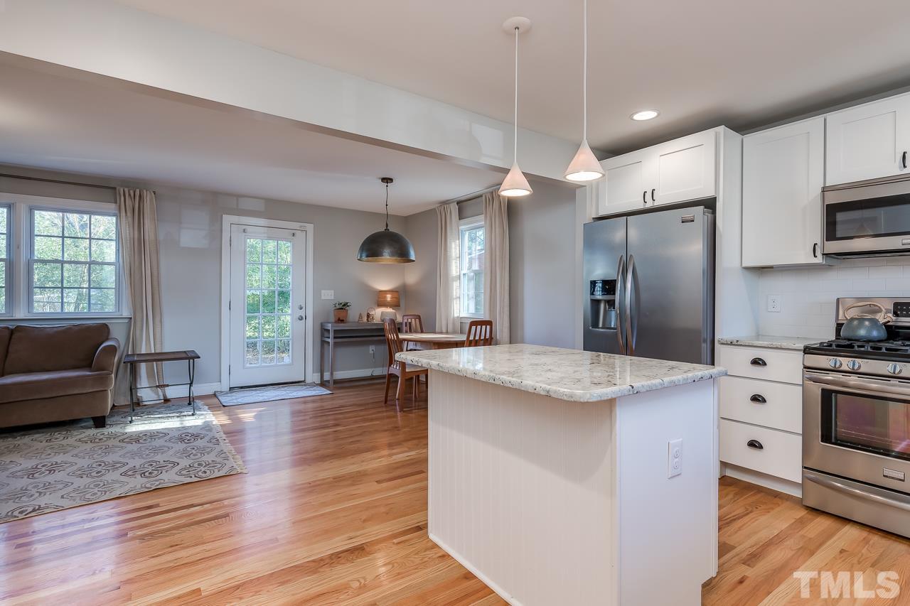 2411 Boswell Road Raleigh, NC 27610 - Photo 7 of 26 a kitchen view with stainless steel appliances kitchen island granite countertop a stove a refrigerator a dining table and chairs with wooden floor