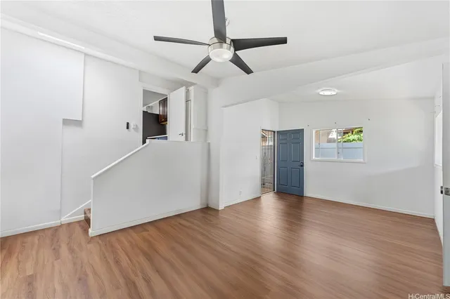 a view of an empty room with wooden floor and a ceiling fan