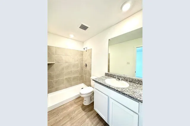 a bathroom with a granite countertop sink a toilet a mirror and shower