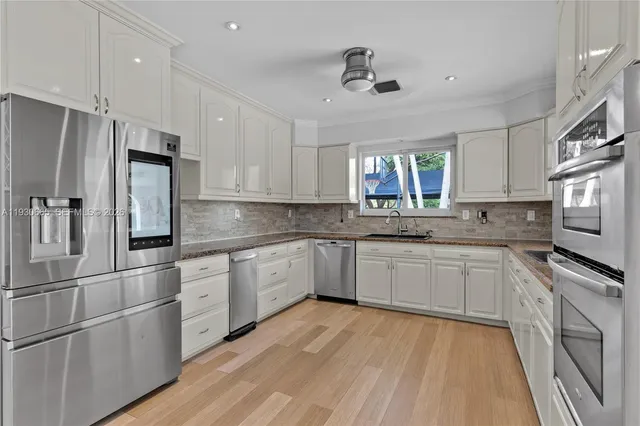 a kitchen with stainless steel appliances granite countertop a stove a sink dishwasher a refrigerator and white cabinets with wooden floor