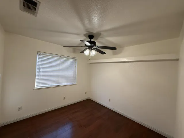 an empty room with wooden floor chandelier fan and windows