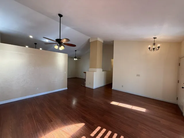 a view of an empty room with wooden floor kitchen view