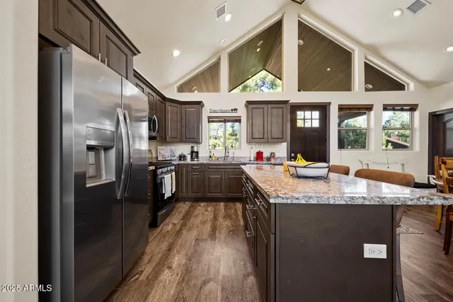 a kitchen with stainless steel appliances granite countertop a refrigerator a sink dishwasher a stove and a dining table with wooden floor