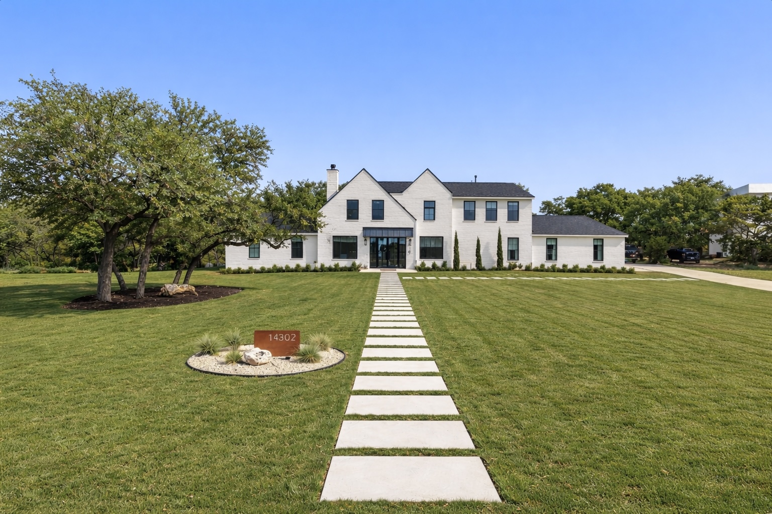 The property features a large, well-maintained lawn, a paved driveway, and mature trees