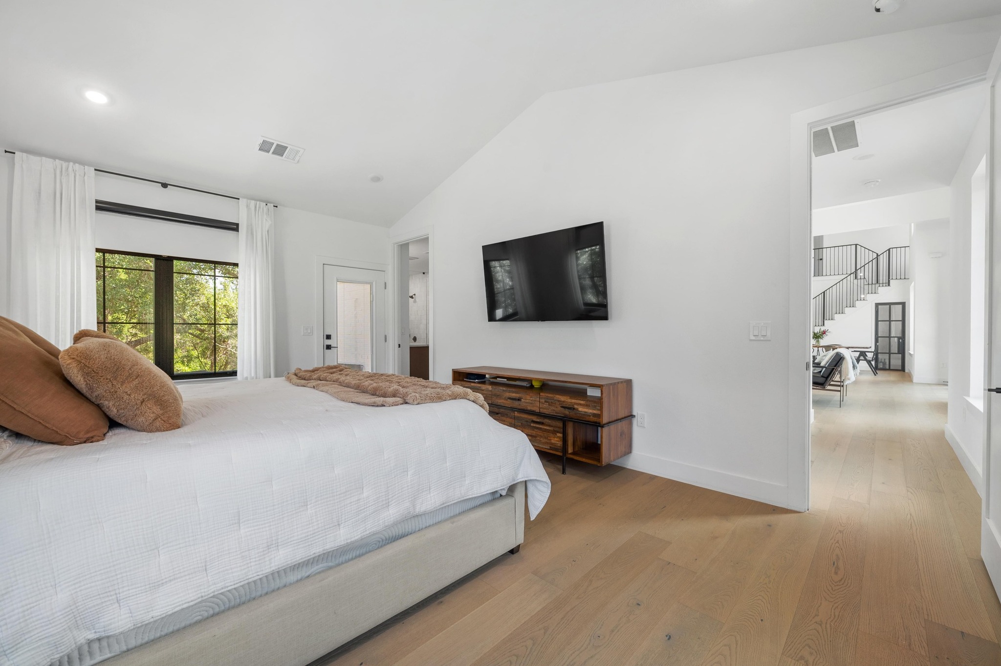 14302 Fallen Timber Drive Austin, TX 78734 - Photo 12 of 37 Spacious bedroom featuring light hardwood floors, a large window with a view of greenery, and a white door providing direct access to an outdoor area