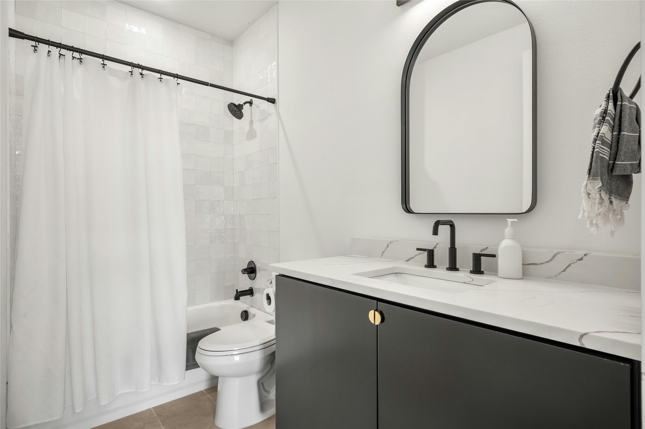 14302 Fallen Timber Drive Austin, TX 78734 - Photo 20 of 37 Bathroom featuring a bathtub with a shower, a dark-toned vanity with gold-toned hardware, a light-toned countertop, and a contemporary mirror