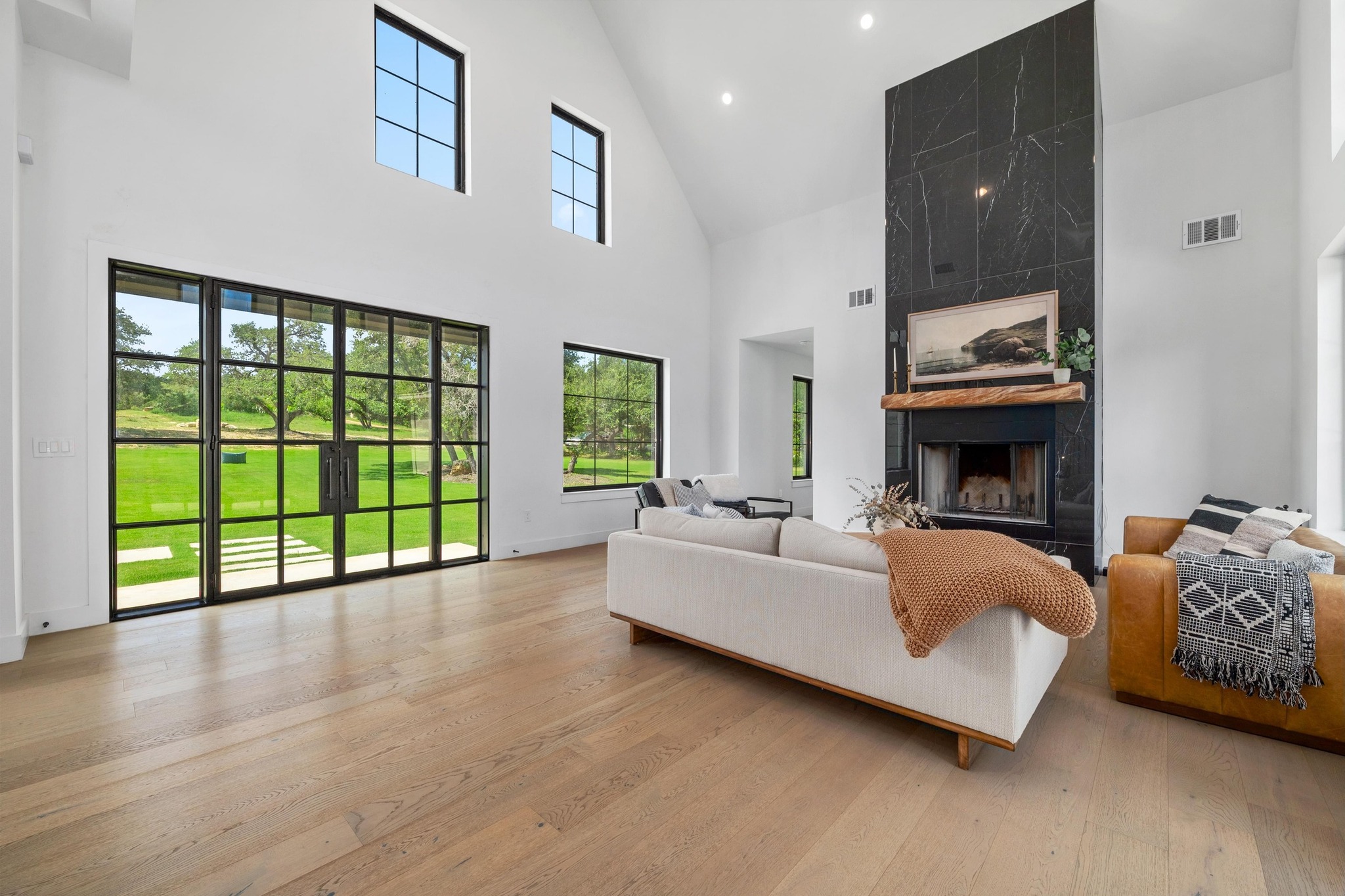 14302 Fallen Timber Drive Austin, TX 78734 - Photo 2 of 37 Spacious living area featuring light-toned hardwood flooring, a tall vaulted ceiling, and substantial windows with views of a green lawn and trees