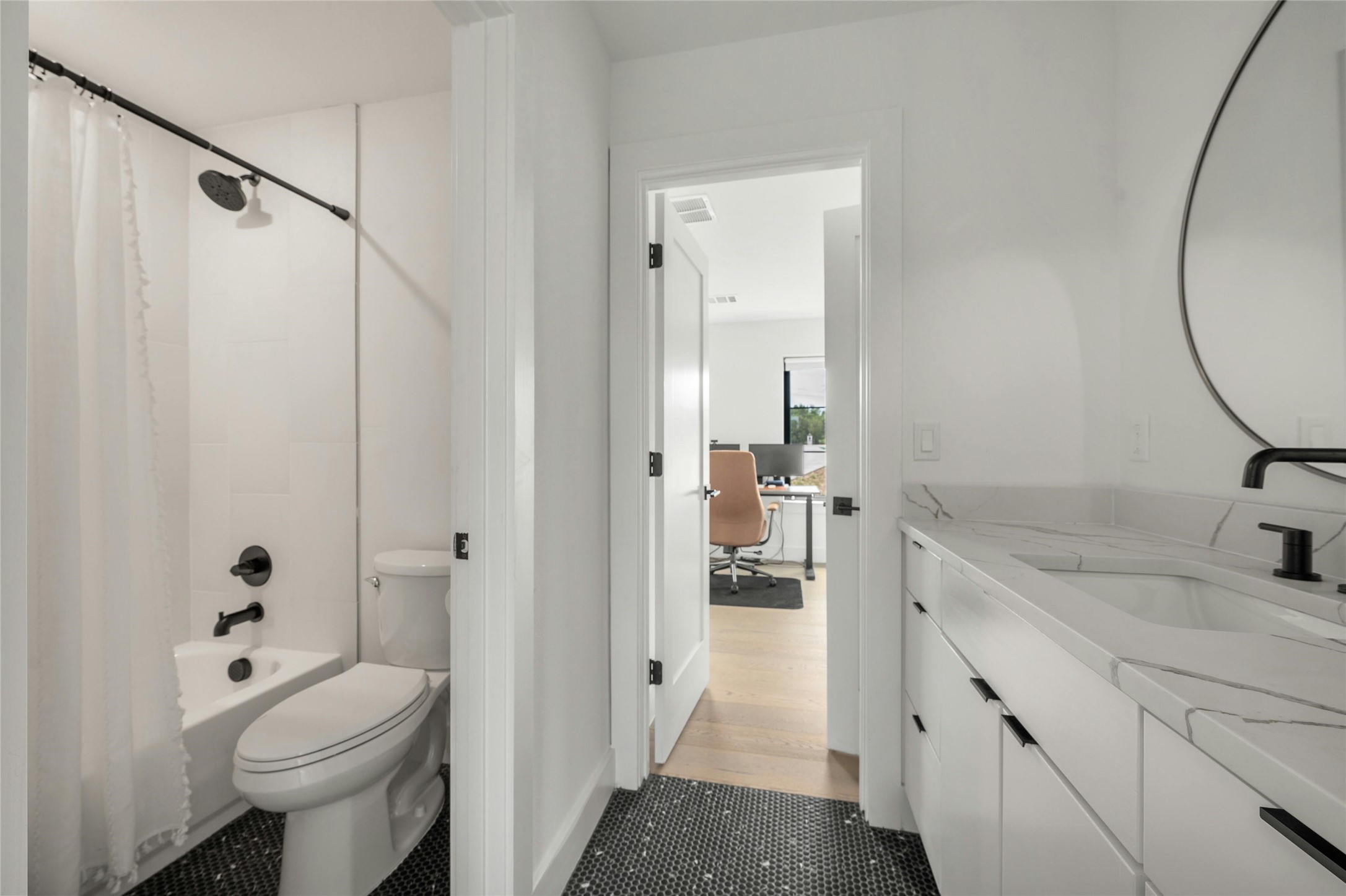14302 Fallen Timber Drive Austin, TX 78734 - Photo 25 of 37 The bathroom features a vanity with a white countertop and integrated sink, a round mirror, and a bathtub with a shower