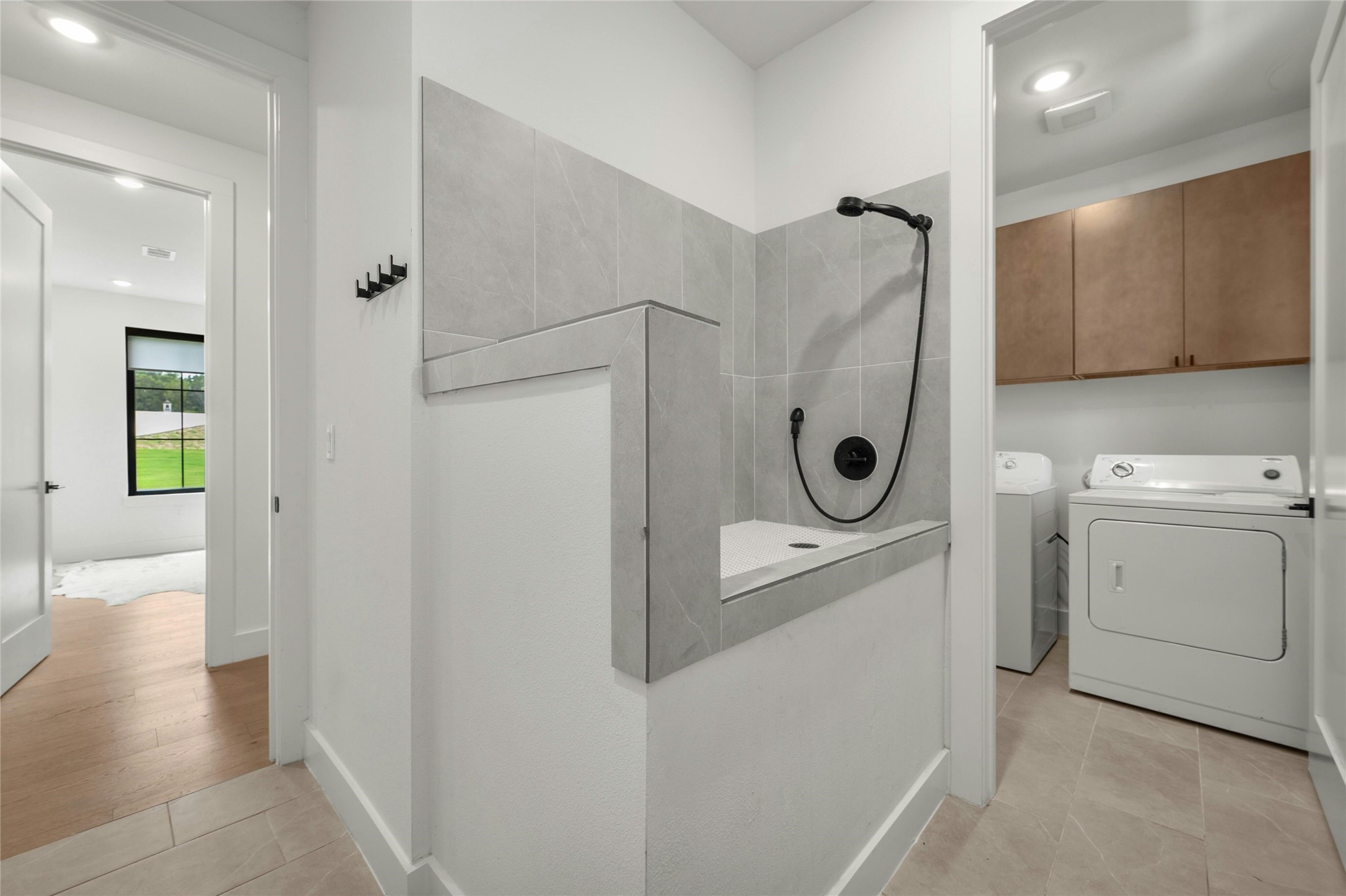 14302 Fallen Timber Drive Austin, TX 78734 - Photo 27 of 37 Utility area featuring a tiled wash basin with a showerhead, a washer, a dryer, and overhead cabinetry