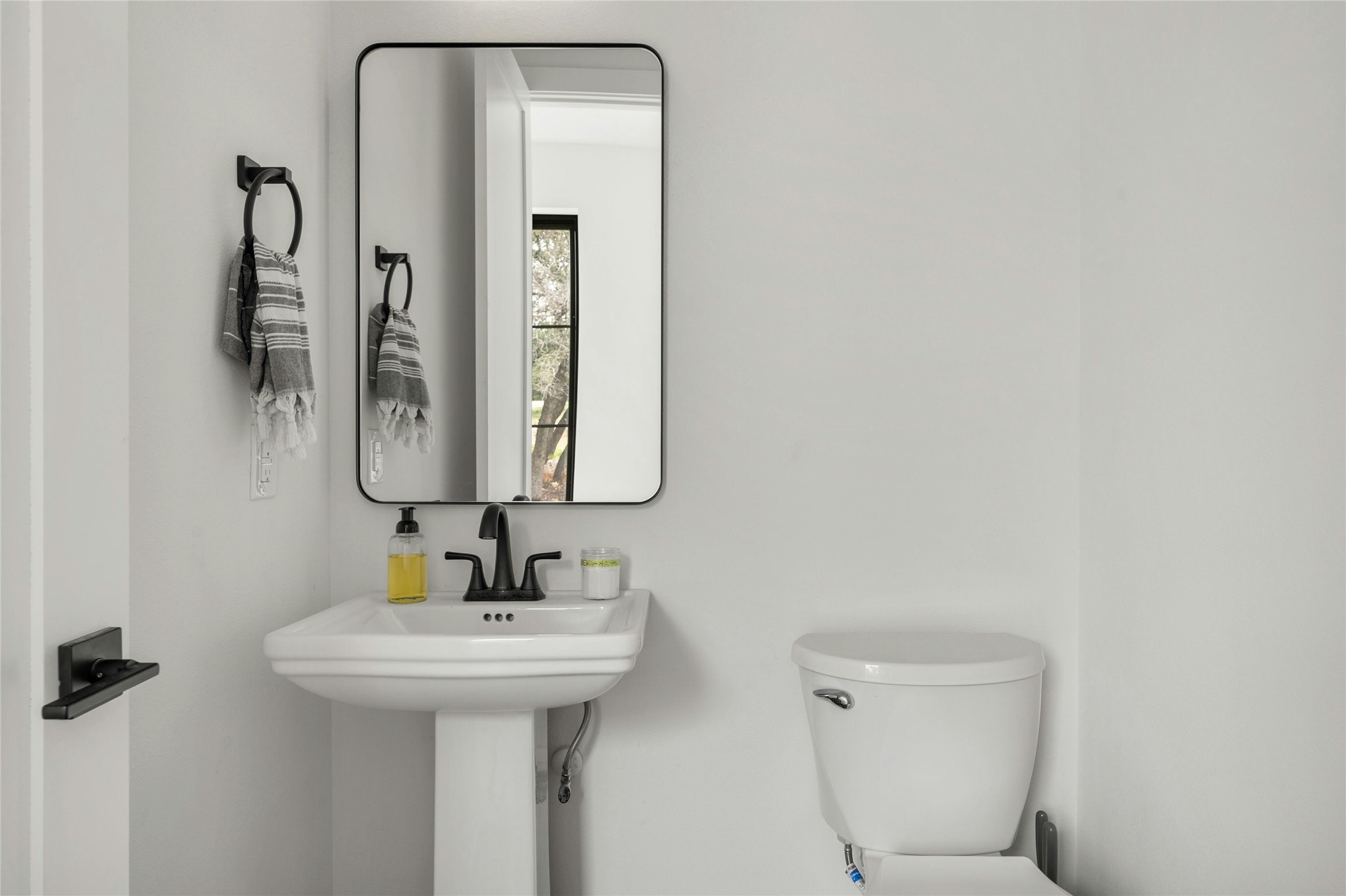 14302 Fallen Timber Drive Austin, TX 78734 - Photo 28 of 37 This powder room features a white pedestal sink with a dark-toned faucet, a framed mirror, and a white toilet