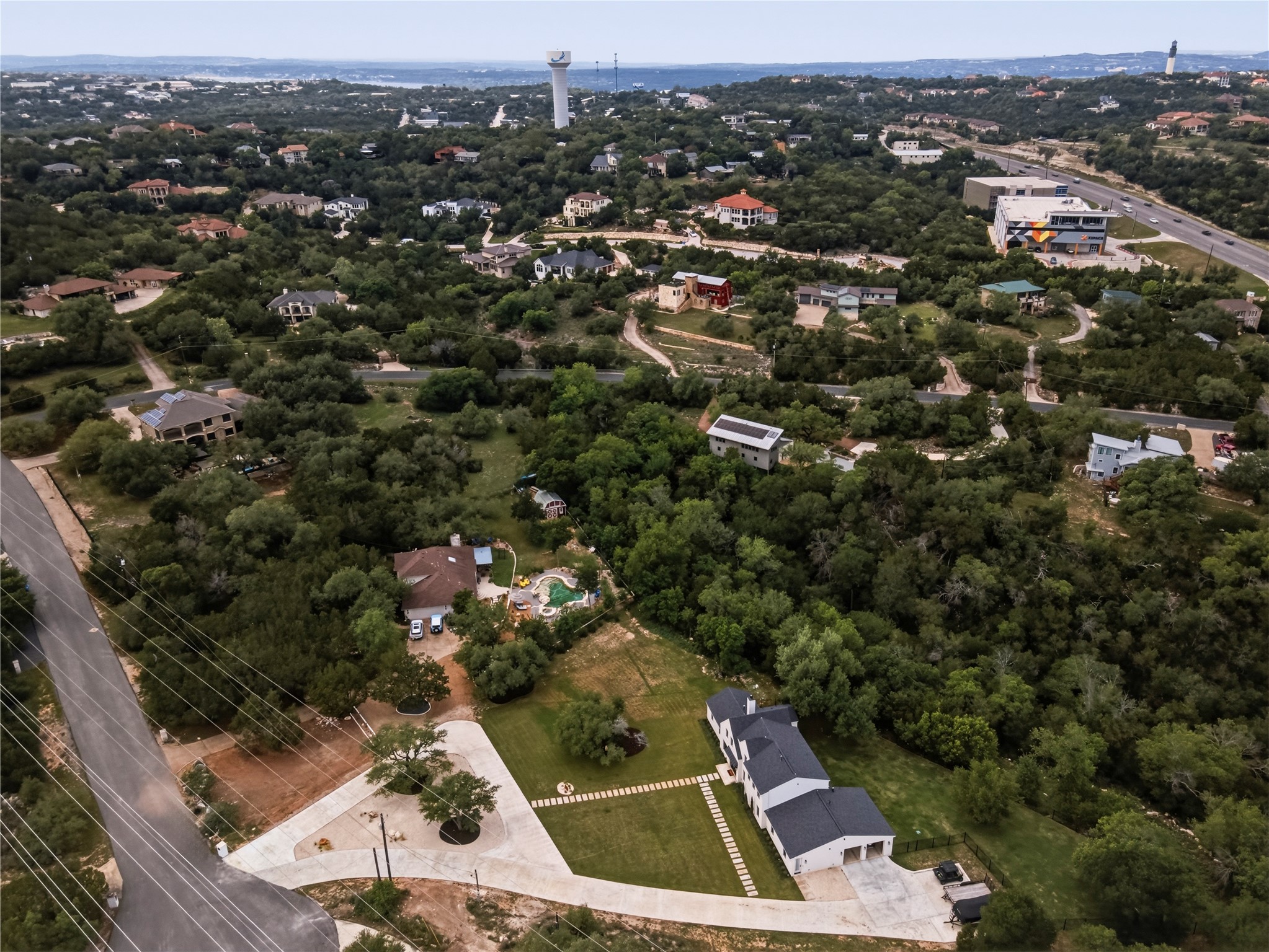 14302 Fallen Timber Drive Austin, TX 78734 - Photo 35 of 37 The property features a large dwelling with a dark roof and a paved driveway leading to an attached garage, set amidst lush green landscaping