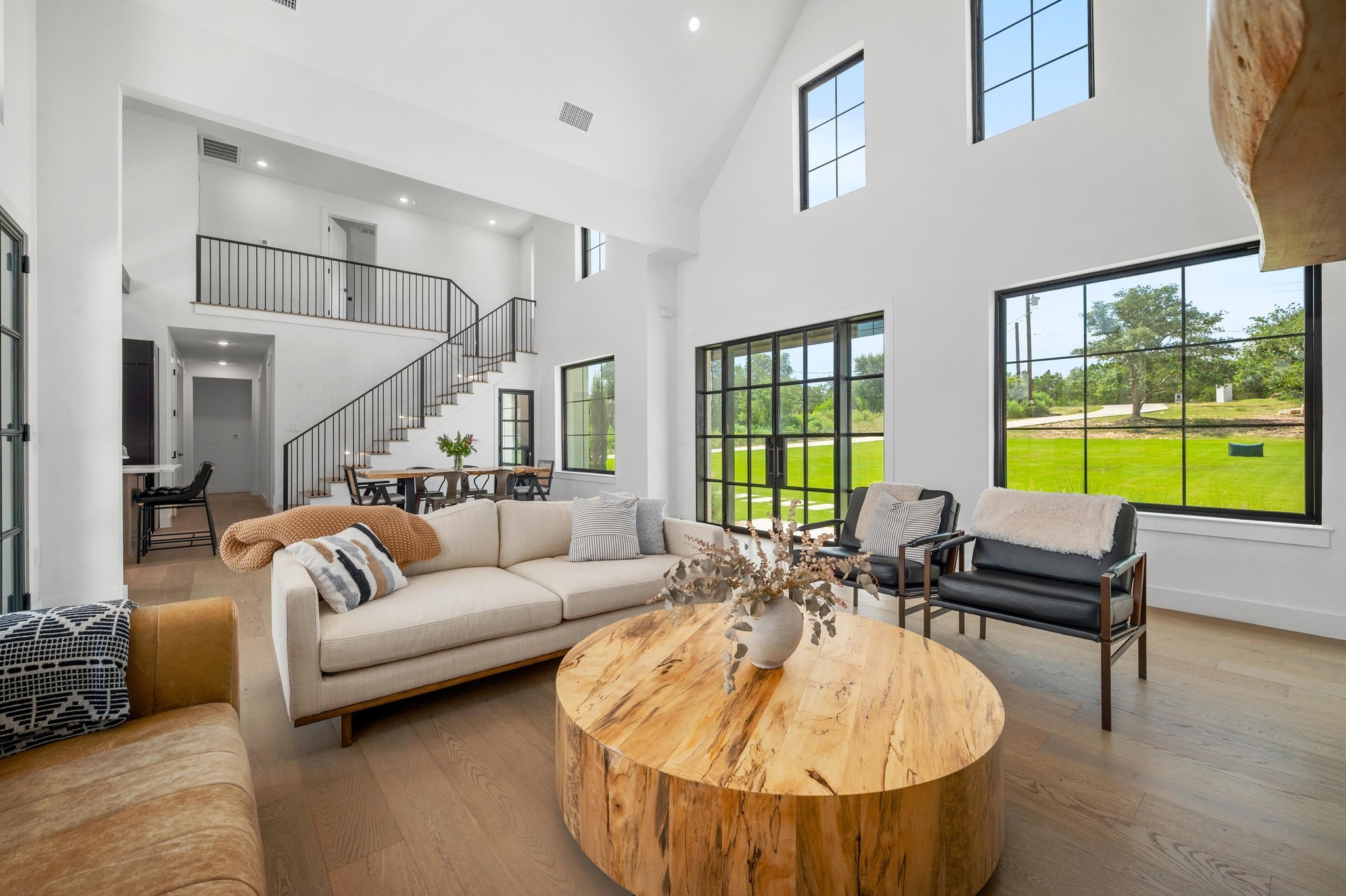 14302 Fallen Timber Drive Austin, TX 78734 - Photo 4 of 37 The living area features high ceilings, hardwood floors, large windows with views of greenery, and a staircase with a black metal railing