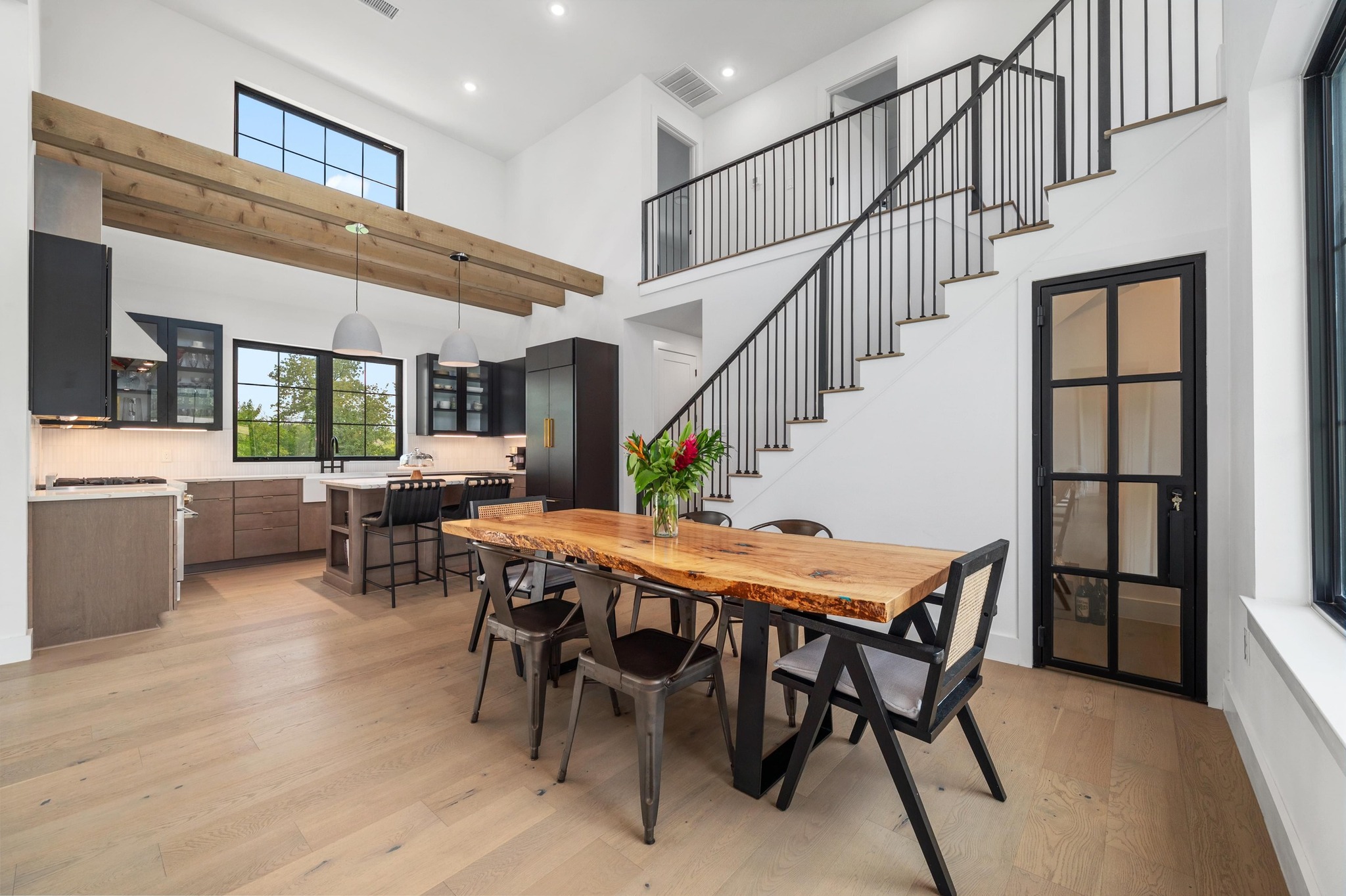 14302 Fallen Timber Drive Austin, TX 78734 - Photo 5 of 37 Open-concept living area with light-toned wood flooring, a kitchen featuring dark cabinetry and a central island with bar seating, and a dining area with a distinctive live-edge wood table