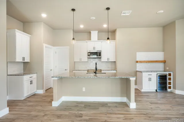 a large kitchen with stainless steel appliances kitchen island granite countertop a refrigerator a stove and white cabinets with wooden floor