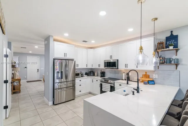 a kitchen with stainless steel appliances kitchen island granite countertop a refrigerator a sink a stove and white cabinets with wooden floor