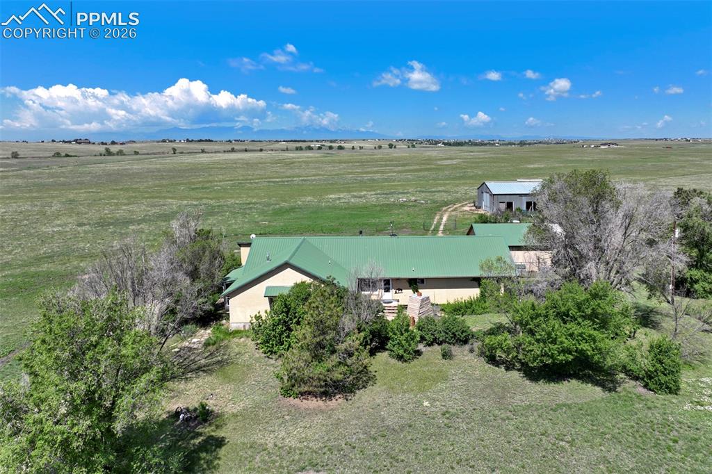 Expansive property featuring a single-story residence with a green metal roof, a detached outbuilding, and significant acreage