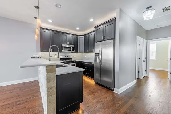 a kitchen with stainless steel appliances granite countertop a refrigerator a sink a stove and a wooden floors