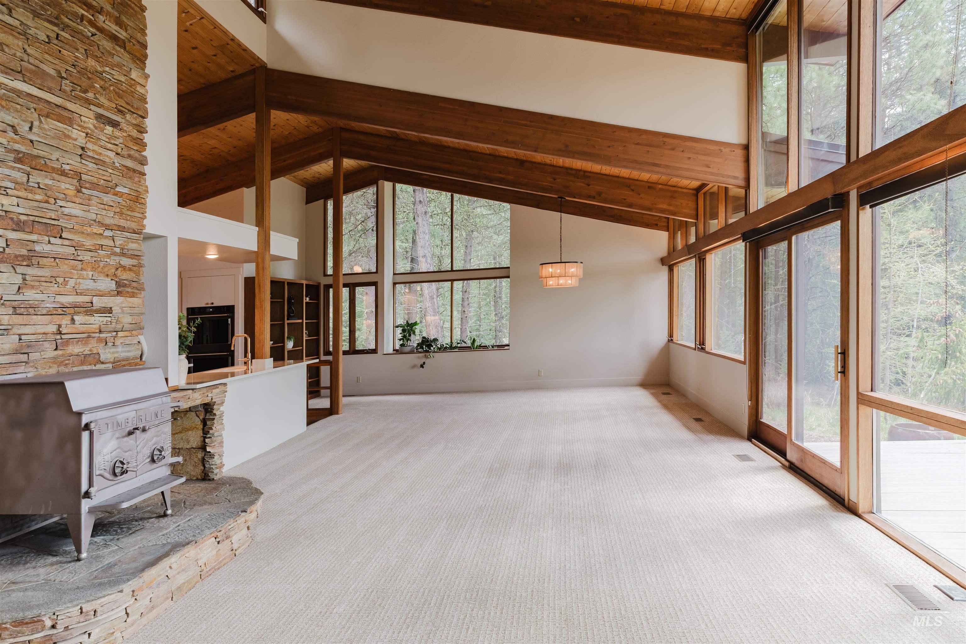 136 Silver Fox Trail McCall, ID 83638 - Photo 11 of 31 Spacious living area featuring a vaulted wood-finish ceiling with exposed beams, a stacked stone fireplace with a raised hearth, a wood-burning stove, and a wall of floor-to-ceiling windows