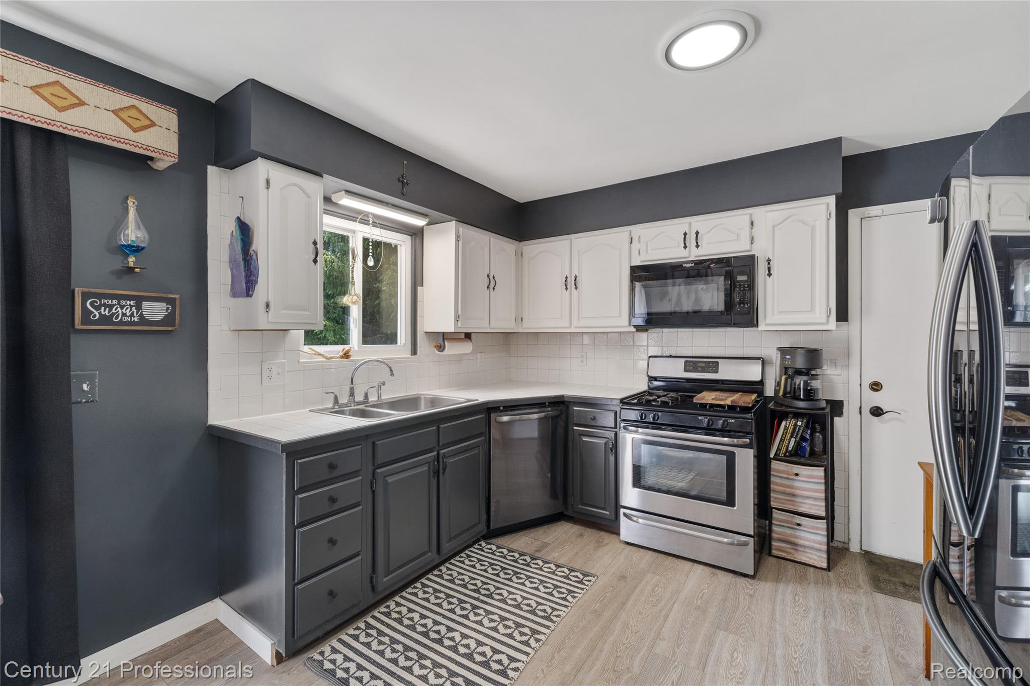 15037 Hogan Road Linden, MI 48451 - Photo 10 of 38 Kitchen featuring wood-finish flooring, two-tone cabinetry, stainless steel appliances, a tile backsplash, and a double-basin sink