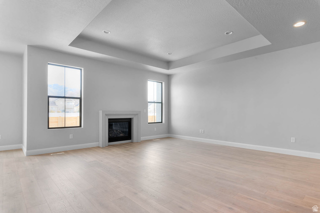 11673 South Halls Crk Road Draper, UT 84020 - Photo 9 of 22 Spacious interior featuring a contemporary fireplace with a stone surround, recessed lighting, a tray ceiling, wood-finish flooring, and multiple windows