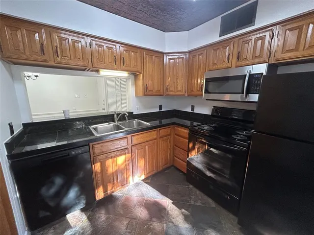 a kitchen with granite countertop a stove top oven a sink and dishwasher a refrigerator with wooden cabinets