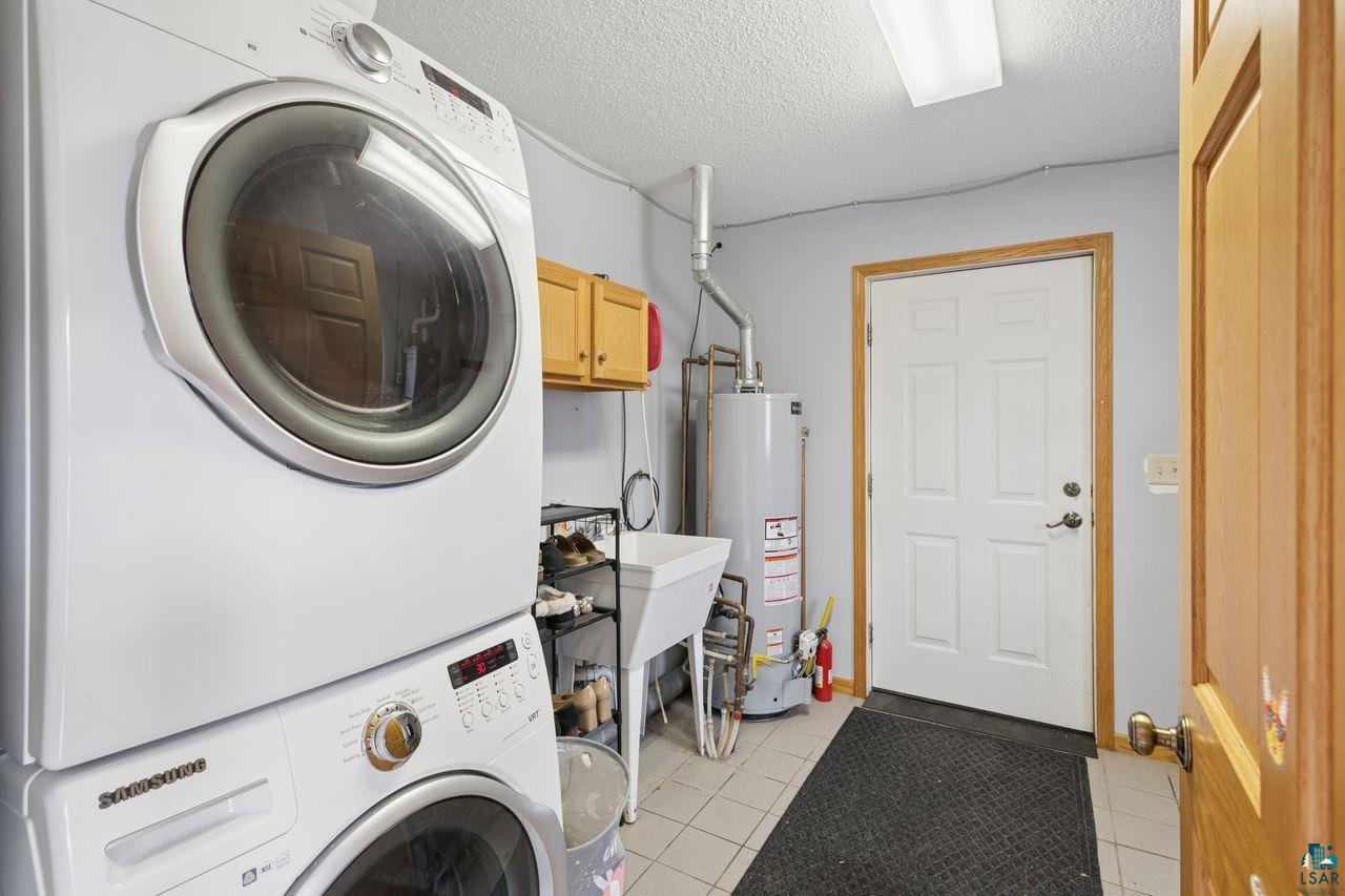 202 Prentice Heights Road Ashland, WI 54806 - Photo 16 of 28 Utility room featuring a stacked washer and dryer, a utility sink, light wood cabinetry, and tiled flooring