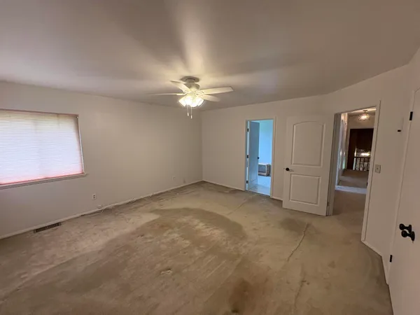 an empty room with chandelier fan and windows