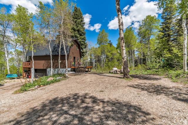 11237 East Aspen Road, Unit 74 Heber City, UT 84032 - Photo 31 of 32 Wood-sided residence with a dark metal roof, featuring a gravel driveway and surrounding mature trees