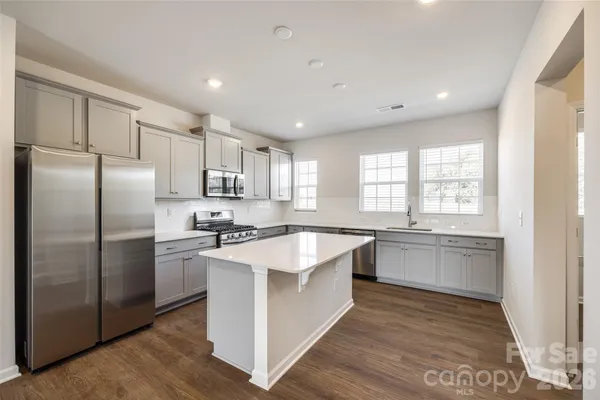 a large kitchen with stainless steel appliances granite countertop a stove a sink dishwasher a refrigerator and white cabinets with wooden floor