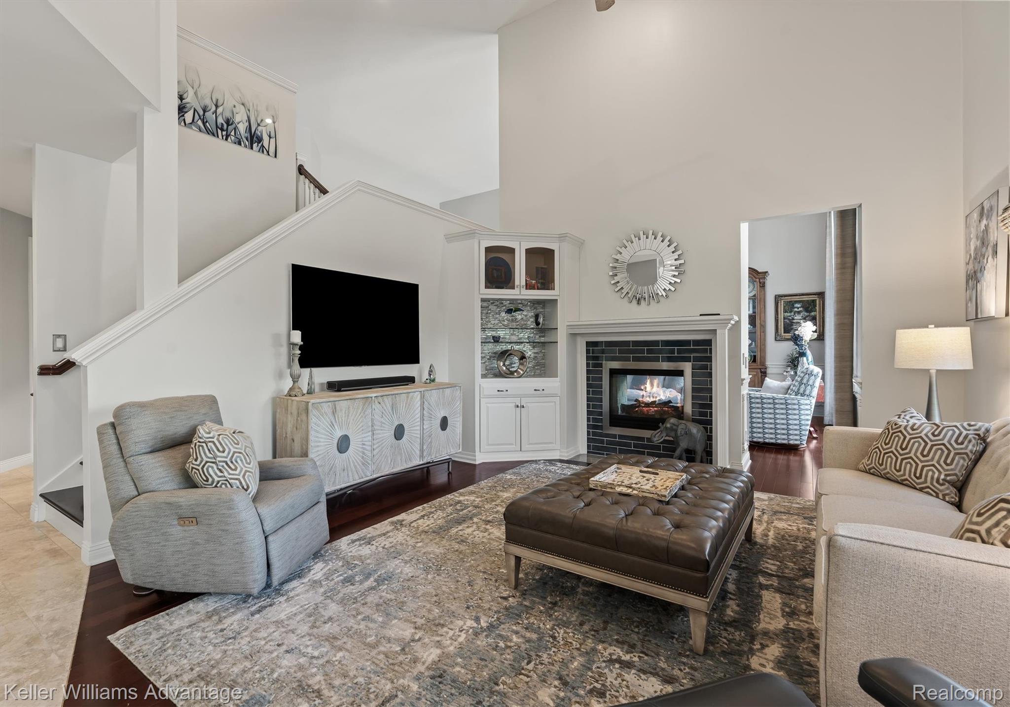 22878 Tree Top Court South Lyon, MI 48178 - Photo 6 of 75 Spacious living area featuring high vaulted ceilings, rich wood-finish flooring, a contemporary fireplace with dark tile surround and white mantel, built-in display cabinetry, and a staircase with white balusters and wood handrail