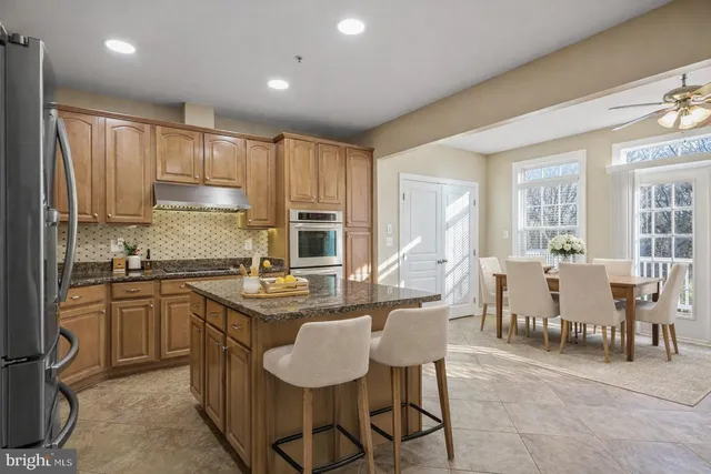a kitchen with stainless steel appliances granite countertop a table chairs sink refrigerator and cabinets