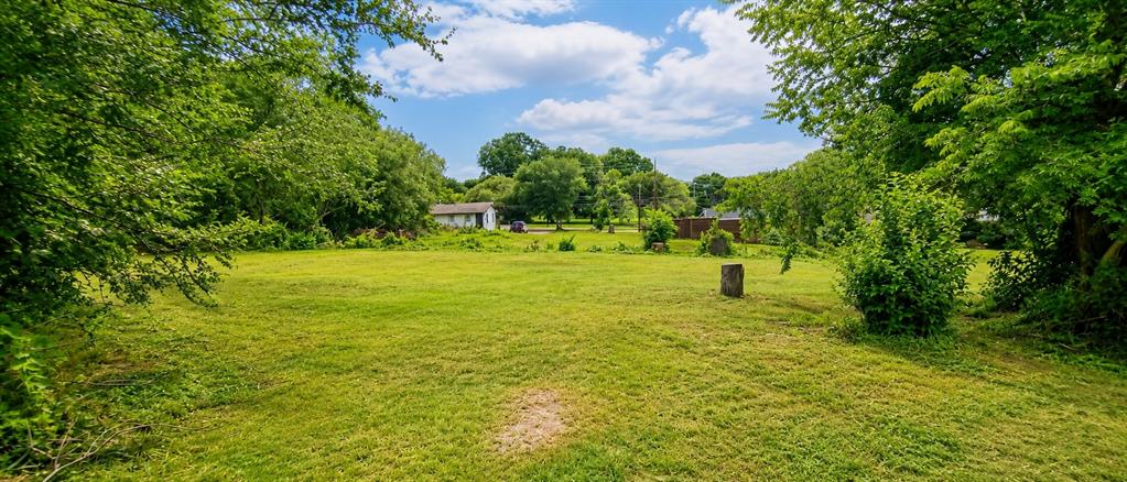 504 North Hampton Road DeSoto, TX 75115 - Photo 6 of 11 Expansive green space featuring a large lawn area, mature perimeter trees, distant structure, and bright sky